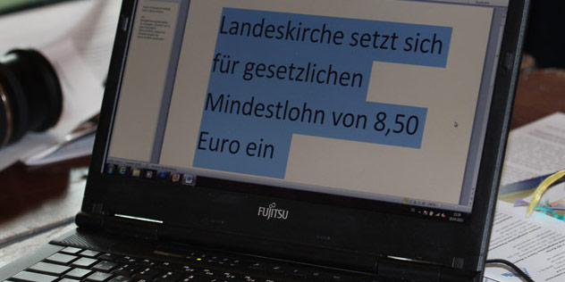 Das Bild zeigt einen aufgeklappten Laptop, auf dem in Großbuchstaben die Mitteilung steht, dass sich die Landessynode für einen Mindestlohn in Höhe von 8,50 Euro einsetzt. Statement der Synode zum Thema Mindestlohn.